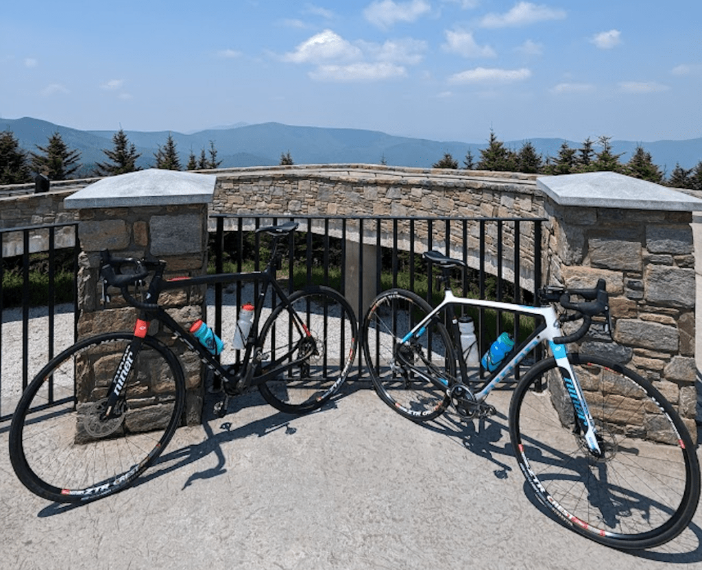 Two bikes leaned up against a fence with mountains in the background