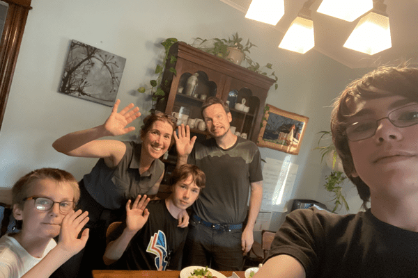 a family standing around dinner table waving
