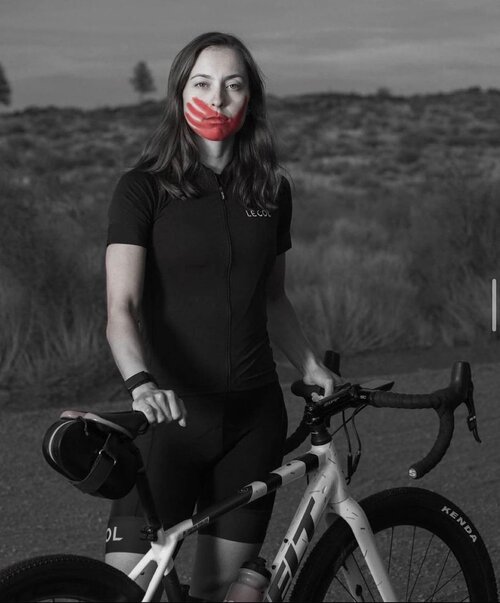Woman standing with bike with red hand print over mouth symbolizing plight of native americal women