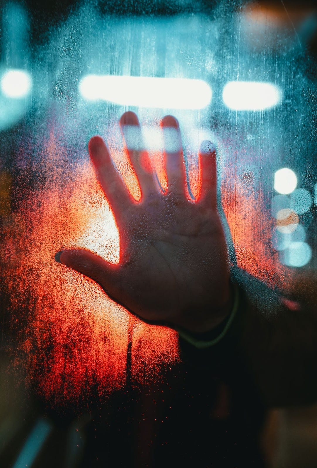 Picture of a hand on a window with red and blue background shining through